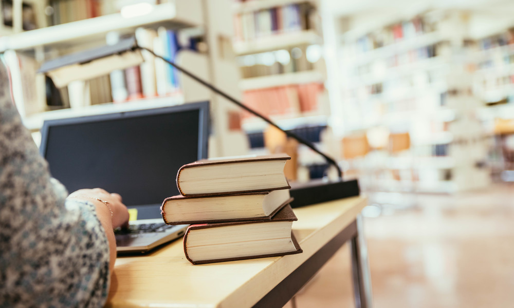 Learning for exams: Blonde female student in the university library, pile of books