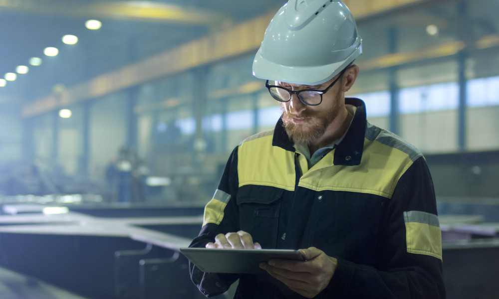 Engineer in hardhat is using a tablet computer in a heavy industry factory.