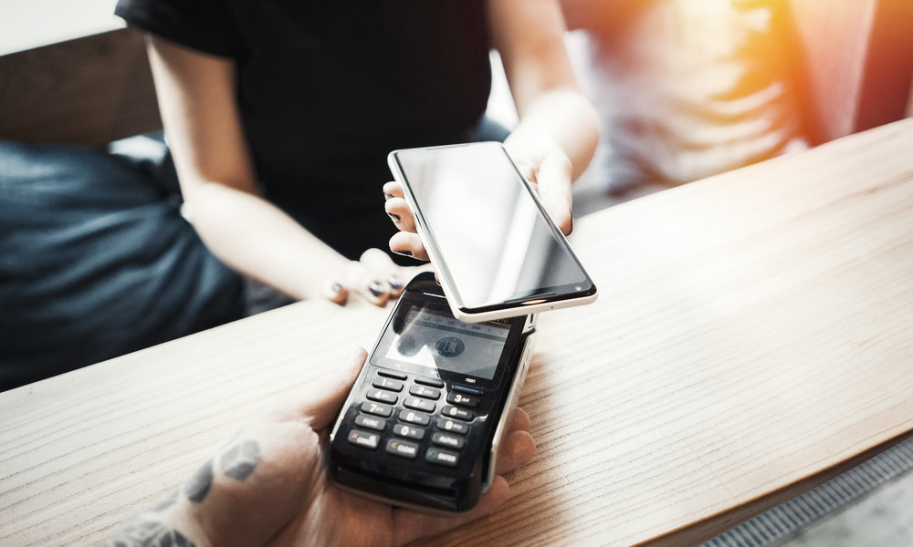 Young woman pays via payment terminal and mobile phone.